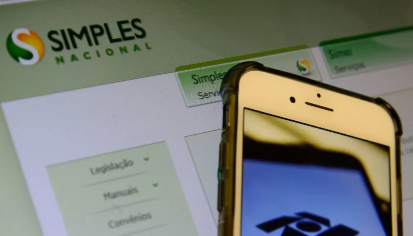 A foto mostra uma tela com o site do Simples Nacional aberto e um celular na frente, com o símbolo da receita federal na tela.